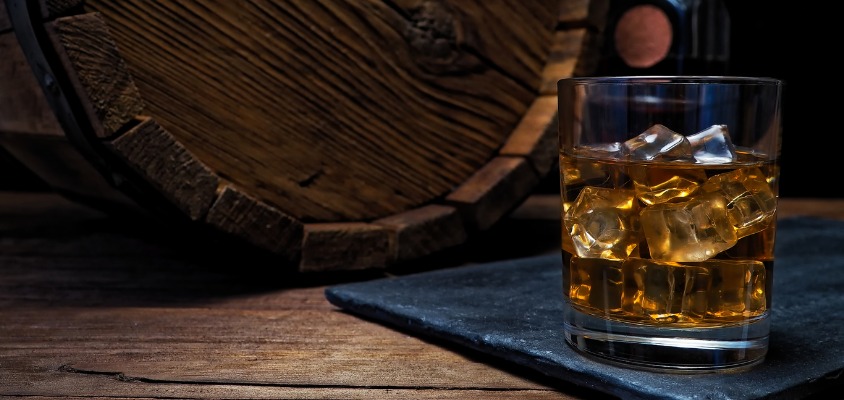 A big glass of Kilchoman whiskey sitting on a bar in front of an oak barrel